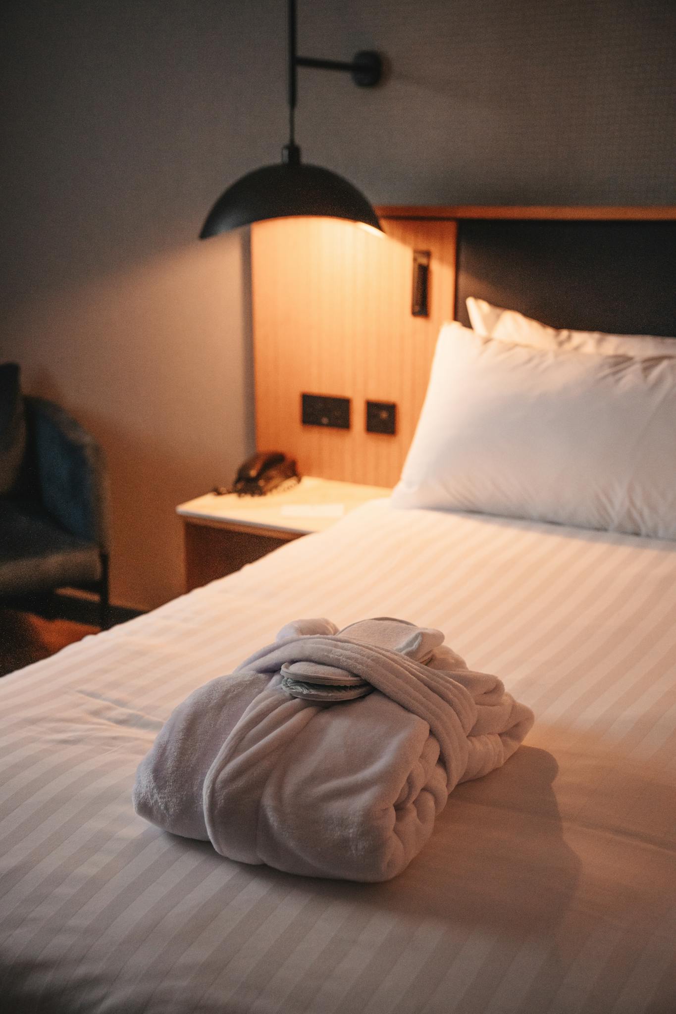 A cozy hotel room featuring a plush robe on the bed under warm lighting, epitomizing comfort and relaxation.