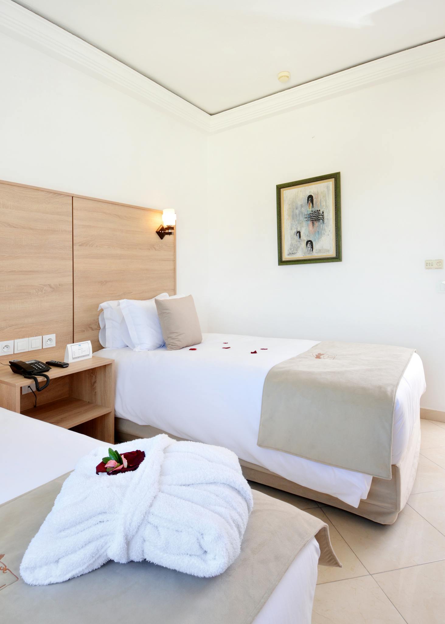 Bright and cozy hotel room featuring twin beds with a framed painting and elegant decor.