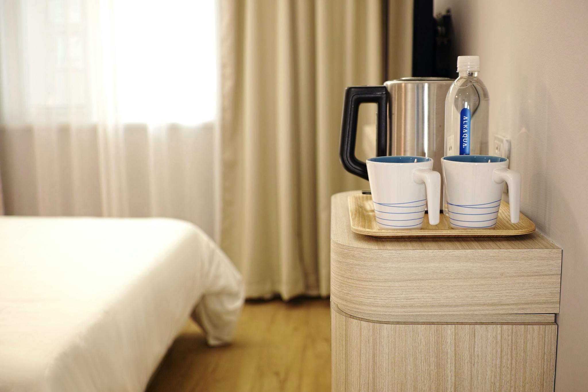 Contemporary hotel room featuring a neatly arranged beverage setup on wooden furniture.